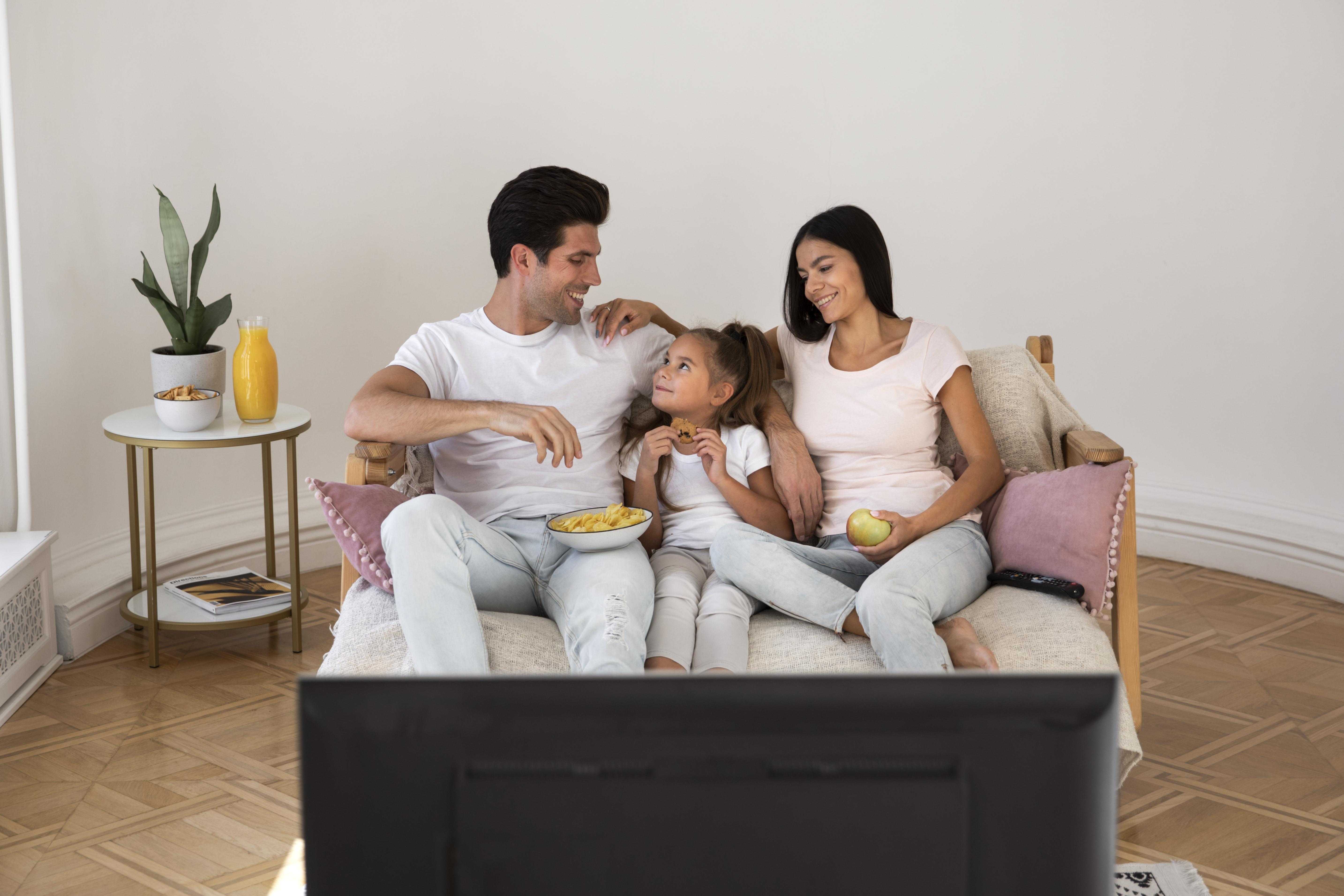Family enjoying IPTV together at home, sitting comfortably and watching TV with snacks in a cozy living room.
